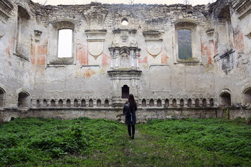 Young slender girl with long blond hair examines the ruins of an ancient synagogue. Traveler with a...
