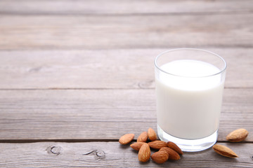 Almond milk in glass with almonds on grey wooden background