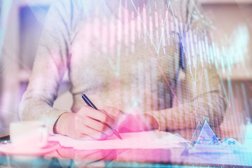 Hand taking notes in notepad. Forex chart holograms in front. Concept of research. Double exposure