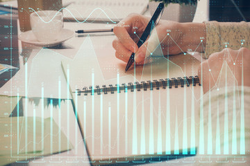Forex chart hologram on hand taking notes background. Concept of analysis. Double exposure