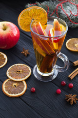 Christmas drink. Mulled wine with apples, orange, cranberries and spices on the black wooden background. Location vertical. Closeup.