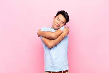 young chinese man feeling in love, smiling, cuddling and hugging self, staying single, being...
