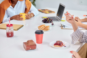 Office workers sit on table during break time, leisure time. Cup of coffee, juice, fruits and cakes on table