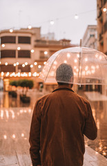 Man under transparent umbrella with lights in background