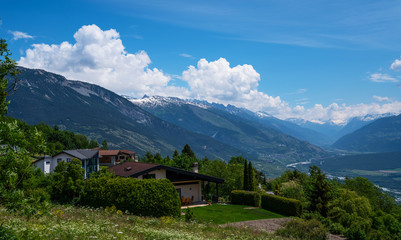 Fototapeta na wymiar Stunning alpine panorama colorful summer view. Beautiful outdoor scene Switzerland, Europe. Hazy blue mountains. Alpine houses, meadows on the slopes and snow-capped mountains.