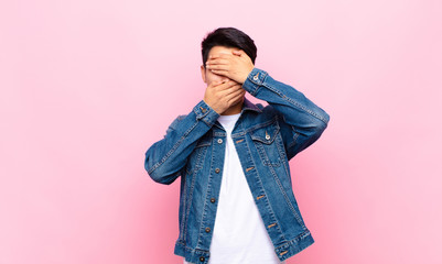 young chinese man covering face with both hands saying no to the camera! refusing pictures or...