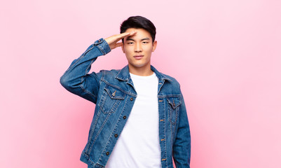 young chinese man greeting the camera with a military salute in an act of honor and patriotism,...