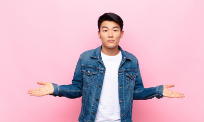 young chinese man feeling puzzled and confused, unsure about the correct answer or decision, trying...