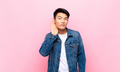 young chinese man looking serious and curious, listening, trying to hear a secret conversation or...