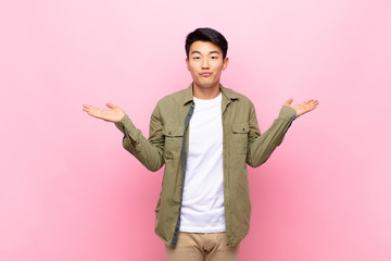 young chinese man feeling puzzled and confused, doubting, weighting or choosing different options...