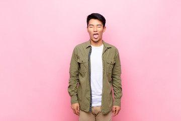 young chinese man with cheerful, carefree, rebellious attitude, joking and sticking tongue out,...