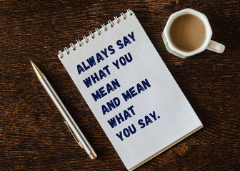 Always say what you mean and mean what you say. Headwriting on a notebook with pen and up of coffee...