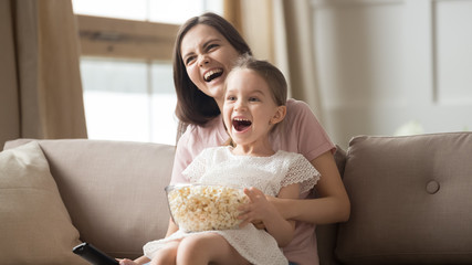 Smiling mom and little daughter watch movie eating popcorn