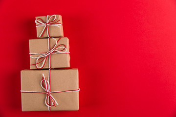 Gifts from craft paper and Christmas tree-shaped ropes on a red background, Christmas concept, greeting card copy space.