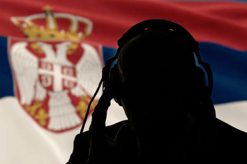Silhouette of a man in headphones on the background of the flag of Serbia, eavesdropping conversation, secret agent, spy and scout, Internet control, backlight