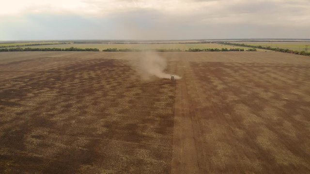 Tractor with harrows working on field cultivating dry soil leaving haystack of dust behind. Drone sliding shot of agricultural machinery with rotary plow prepares land for sowing