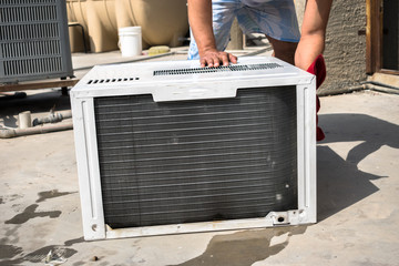 a professional electrician is cleaning the window air conditioner on the roof top of a house with a wet napkin 
