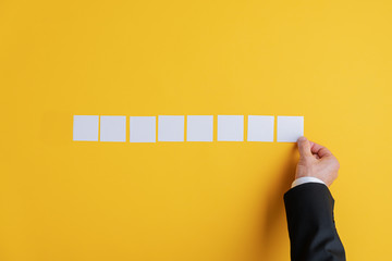 Hand of a businessman placing eight blank white post it papers in a row