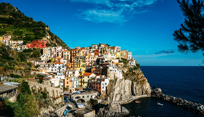 Manarola typical Italian village in National park Cinque Terre, colorful multi colored buildings houses on rock cliff, fishing boats on water, blue sky background, Liguria, Italy