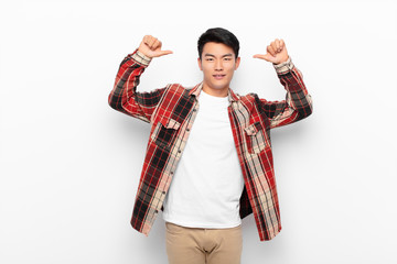young chinese man feeling proud, arrogant and confident, looking satisfied and successful, pointing...