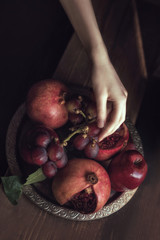 A big plate with red fruits. Grape, garnet, apple. And hand