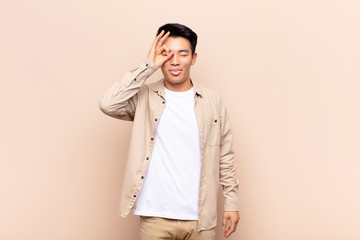 young chinese man smiling happily with funny face, joking and looking through peephole, spying on...
