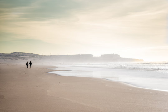 People walking on windswept sunny Guincho beach at low tide