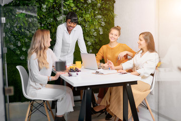 Confident young african lady in white shirt stand talking to caucasian young women, teaching business mentoring, discuss strategy in modern office