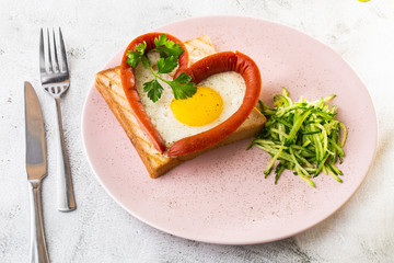 Scrambled eggs in the form of heart on a white plate with sausages, sourdough toast isolated on white marble background. Homemade food. Tasty breakfast. Selective focus. Hotizontal photo.
