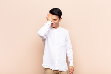 young chinese man laughing and slapping forehead like saying d‚Äôoh! I forgot or that was a...