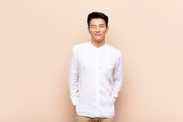 young chinese man looking happy and friendly, smiling and winking an eye at you with a positive...