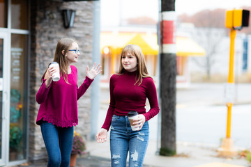 Two young teenager girls going from coffee store. Sisters talking and arguing. Holding coffee cups and drinking.  Casual style, city street