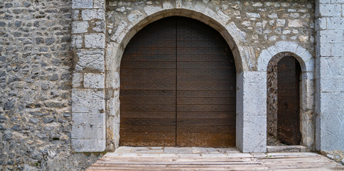 Medieval castle gate. Ancient wooden door in old stone castle wall. Locked wooden door with metal forging.