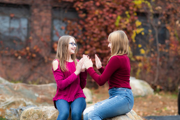 Two young teenager girls sitting on the rock. Sisters, friends happy smiling, laughing, talking....