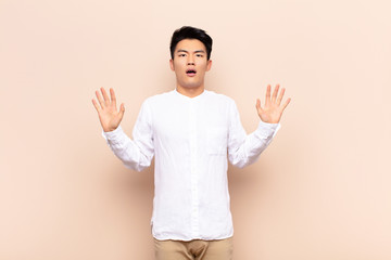 young chinese man feeling stupefied and scared, fearing something frightening, with hands open up...