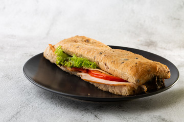 Baguette sandwich with salami, turkey breast, cheese, lettuce, tomatoes and onion on a cutting board. Long subway sandwiches isolated on white marble background.  Selective focus. Horizontal photo.