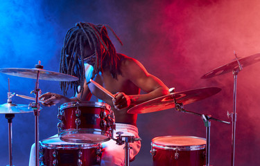 portrait of showy african drummer man with percussion instruments isolated over neon smoky background