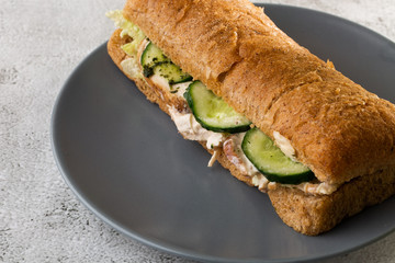 Baguette sandwich with salami, turkey breast, cheese, lettuce, tomatoes and onion on a cutting board. Long subway sandwiches isolated on white marble background.  Selective focus. Horizontal photo.
