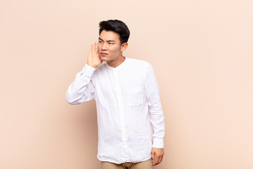 young chinese man looking serious and curious, listening, trying to hear a secret conversation or...