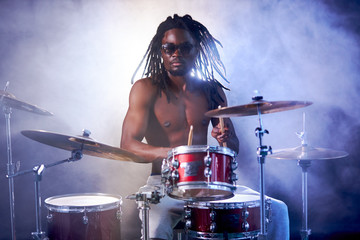 vigorous black man playing on drums with naked skin, wearing eyeglasses, dreadlocks on head,...