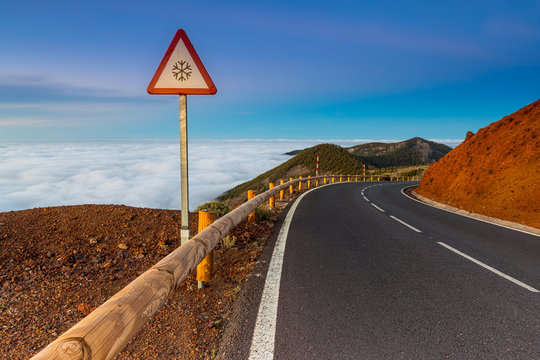 Mountain route above the clouds in Tenerife Island, Spain. Snow danger sign in the middle of a mountain road.