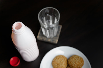 Opened bottle of strawberry or raspberry yogurt standing on black table with glass and cookies. Dairy product. Healthy food and drinks concept. Place for text.
