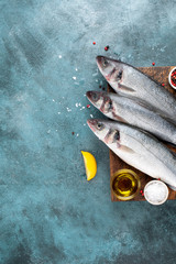 Fresh sea bass fish and lemon, olive oil, salt, pepper on turquoise grunge background. Top view