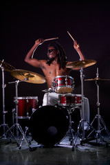 Obraz na płótnie Canvas Portrait of african man playing on drums and cymbals, wearing eyeglasses and holding sticks. isolated over dark background