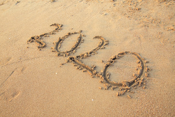 020 text painted on the yellow sand on the beach.