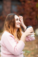 White female, Caucasian woman sitting on rock, holding coffee. Smiling and happy. Autumn, Fall.