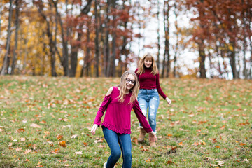 two young beautiful happy teenager girls, sisters and friends playing, running, jumping in forest. Colorful Fall, Autumn