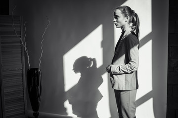 young pretty emotional and sexy girl with blue eyes in a black sweater and red pants stands looking down at her sun's rays, low key 