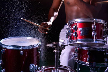 cropped black male with naked skin sit beating drums with sticks, wet drums, wet percussion instruments. drops of water on drum set