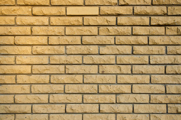 Rustic yellow brick wall. The edge of the brick has been chipped. The upper left corner of the wall is lit by the setting sun. Background. Texture.
